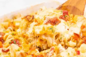 Dish with a spoon full of creamy bacon and ranch pasta with melted cheese. 