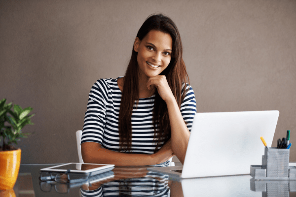 Woman sitting at a desk smiling in front of a white laptop. 