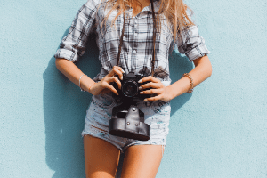 Woman holding a camera leaning against a blue wall. 