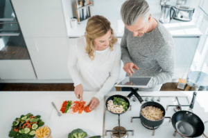 Couple cooking a romantic dinner together at home. Fresh veggies are laid out on the table.