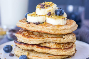 stack of blueberry pancakes with cut up bananas on top. 