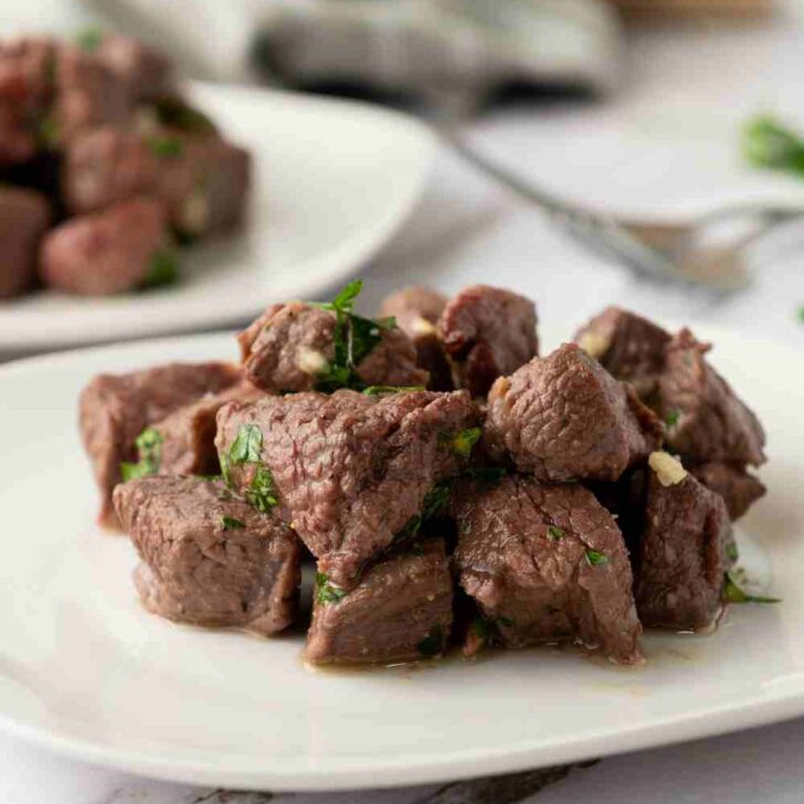 small steak bites piled on a white plate.