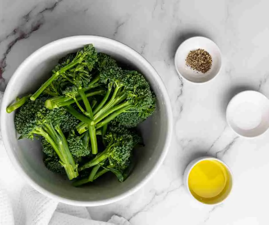 Raw broccoli in a bowl, salt, pepper, olive oil in a bowl. 